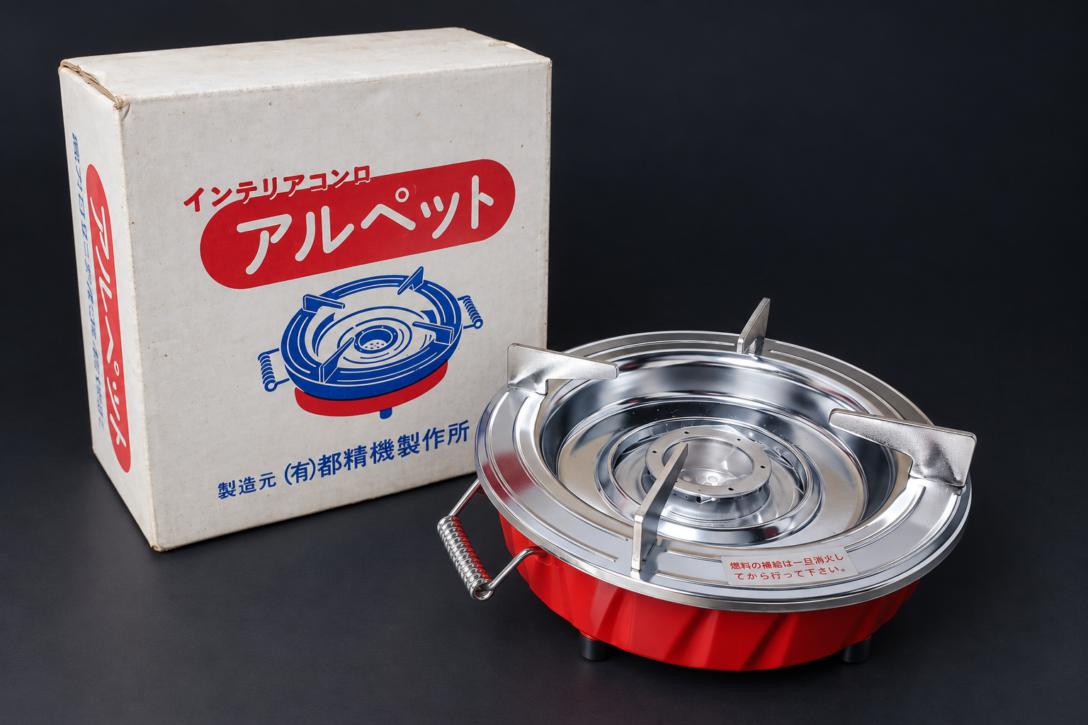 赤い本体と銀色の金属部品を備えたアルコールバーナー「アルペット」。当時の箱と並べた展示イメージ